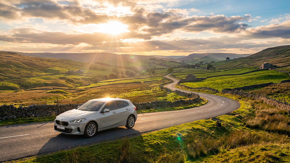 White BMW 1 Series hatchback on a winding road through the Yorkshire Dales at sunset